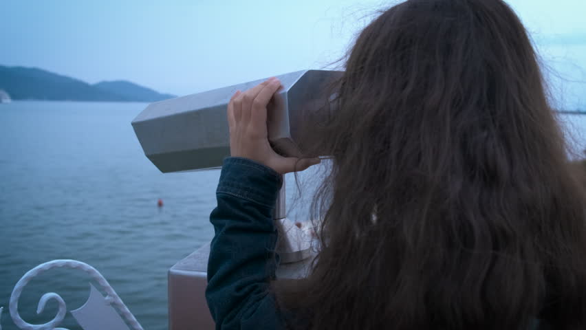 The child looks through binoculars into the sea. A little girl looks through thick binoculars on the observation deck.