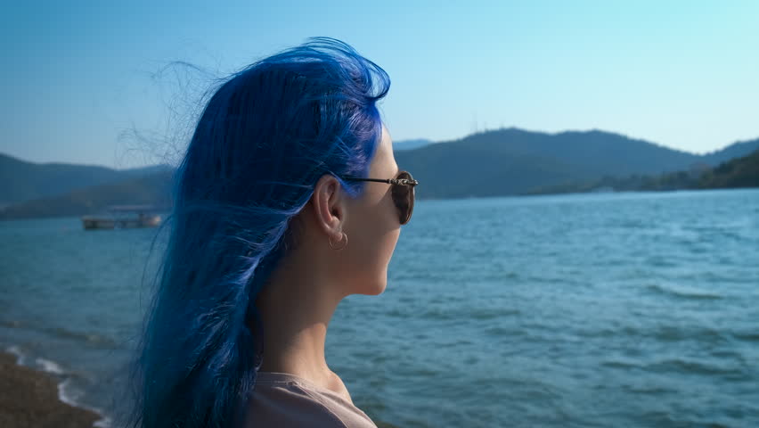 Enjoy the seascape. A girl with blue hair looks into the distance of the turquoise sea.