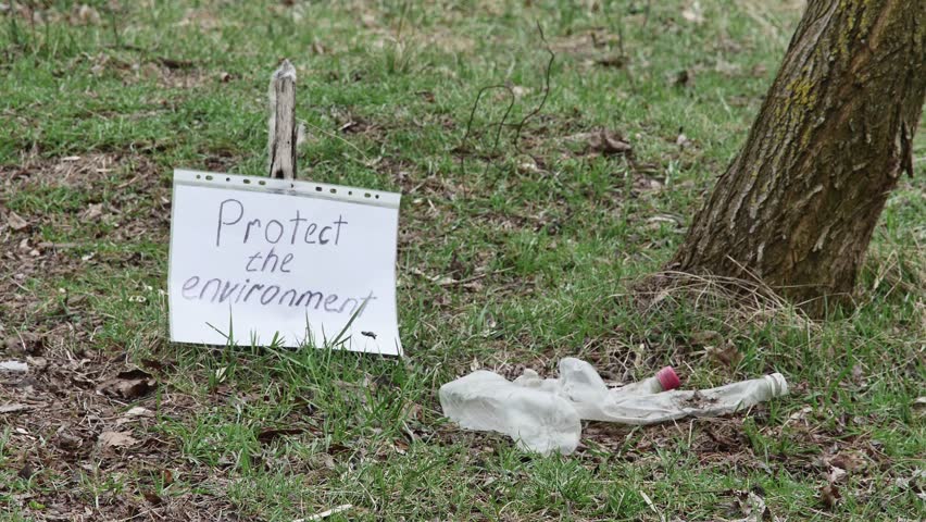 a man in the spring forest bends down and puts old plastic bottles in a plastic garbage bag.