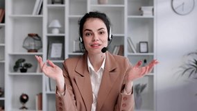 Young curly brunette woman wearing video call headset view from camera in home white office. Video conference, remote meeting. Programmer, remote work, work from home