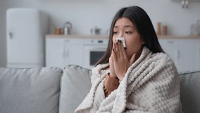 Unhealthy ill sick Asian woman multiethnic korean chinese girl patient covered in warm blanket at home blowing to paper napkin sneeze runny nose allergy flu caught cold sneezing has covid-19 symptom - Powered by Shutterstock - Get 15% off with code: PIKWIZARD15