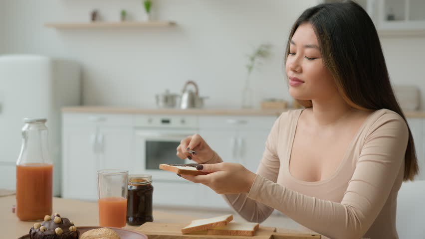 Asian korean japanese woman housewife cooking breakfast in domestic kitchen spread chocolate paste sweet jam on bread put on toast peanut butter with knife ordering food delivery at home eat sandwich Royalty-Free Stock Footage #1101721357