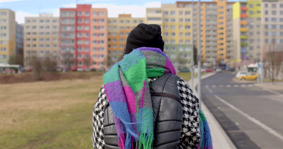 The back of a people is moving along the sidewalk in the city. The movement ball in the wind. Backpack shoulders. Against background multi-storey building in bokeh. Camera movement.