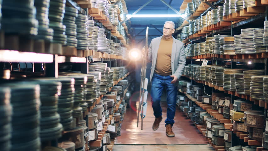 Archive worker is using a ladder to get a case with film reel
