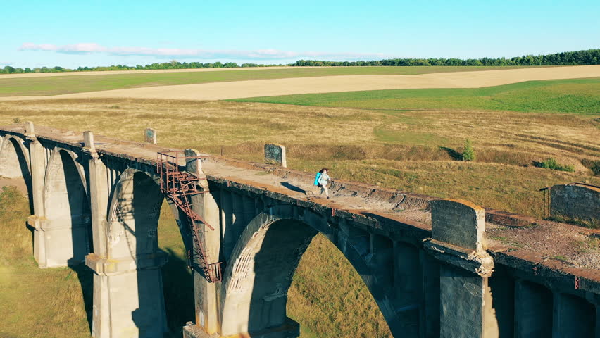 A lady is walking along a deserted bridge with sports inventory