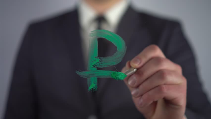 A businessman draws on the glass the currency symbol of the Russian ruble. A man in a suit draws on glass with a brush and green paint.