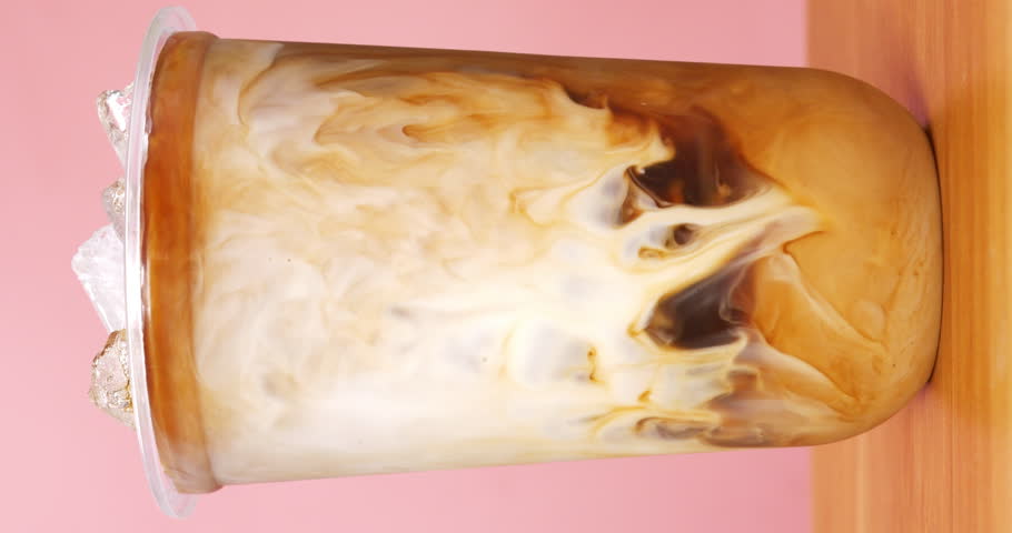 4K footage vertical video front view, flowing milk blending homogenously with coffee in glass on the table, coffee art concept. | Shutterstock HD Video #1101729833
