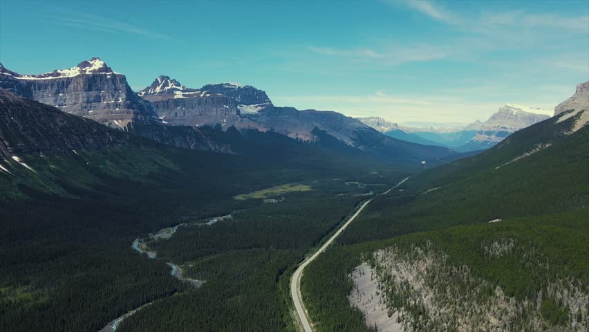 Drone Shot of Scenic Mountains with snow peaks and pine woods in Banff National Park. Lake with turquoise water. Aerial video in mountain over a forest in the Rocky Mountains in Canada.
