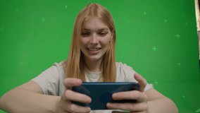 Wide-angle video of a white race cheerful red-haired girl looking at something on a smartphone and smiling on green screen background