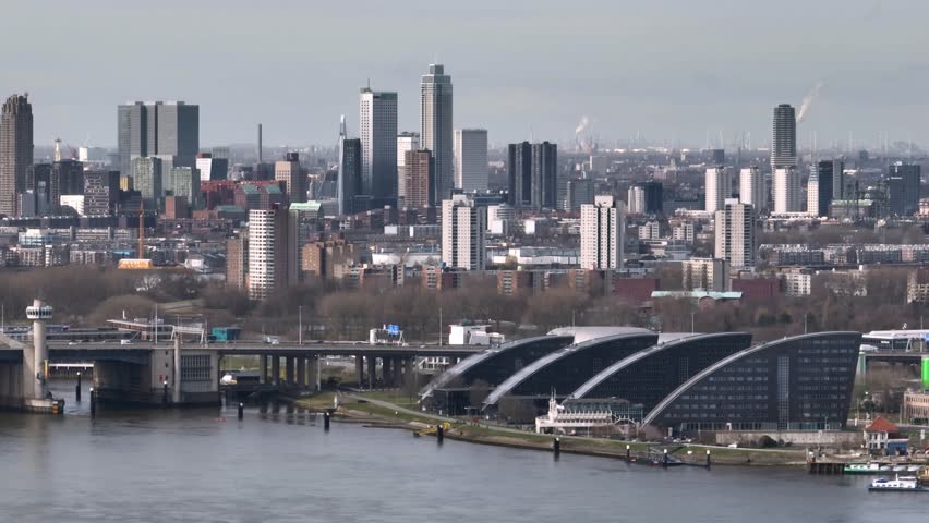 Wide aerial panning shot of the Rotterdam skyline with the Van Brienenoord bridge over the Nieuwe Maas, and vehicle traffic 