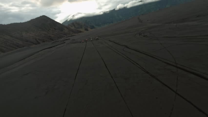 Extreme sport race dirt bike Enduro group approaching volcano on sand lava field aerial view. FPV drone shot speed cross motorcycle rider travel competition natural volcanic area flip freestyle trick | Shutterstock HD Video #1101749563