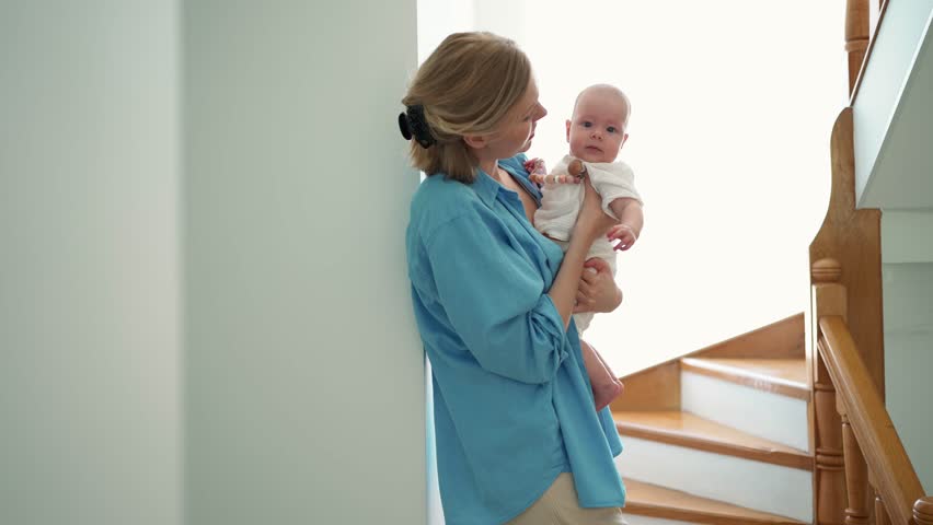 Happy blonde mother talking with a small child in her arms indoors at home