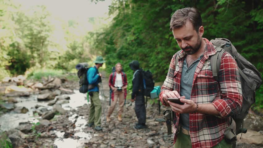 Concentrated brunet tourist man typing on mobile and looking at his friends in the mountains outdoors Royalty-Free Stock Footage #1101750027