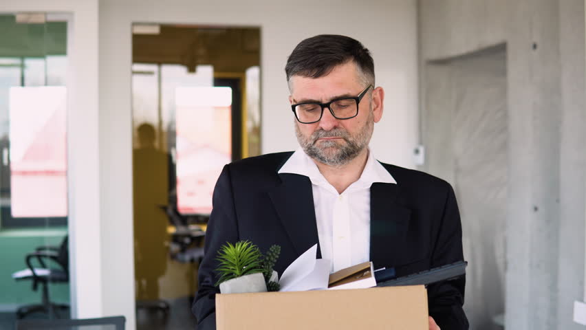 Sad dismissed senior worker are taking his office supplies with him from office. Old man is retiring. Retirement concept. Dismissal from work Royalty-Free Stock Footage #1101751245