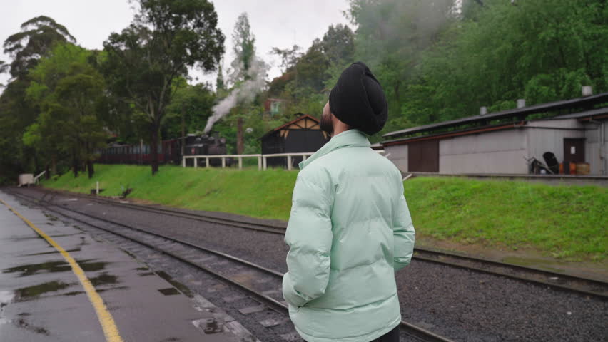 Rear Of An Indian Sikh Man Standing Near The Railway With Steam Train At Background. Medium Shot