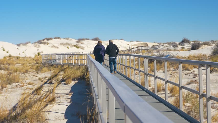 Old married couple walking hiking seeing sights on trail deck with sand dunes at white sands national park in New Mexico, USA