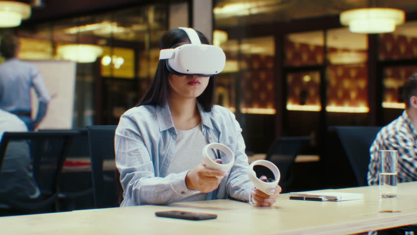 Female office worker uses VR headset and wireless controllers, watches data and numbers in 3D virtual reality. Asian woman works in modern hi-tech IT company. Future innovative digital technologies. Royalty-Free Stock Footage #1101759235