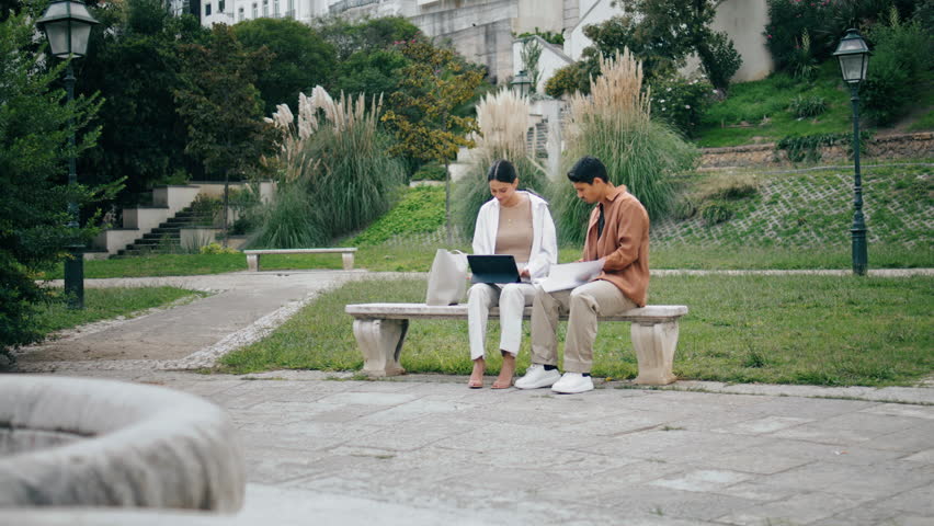 College students learning tablet on bench. Inspired young business couple using tab computer working in green park zone. Confident colleagues checking documents talking outdoors. Teamwork concept 