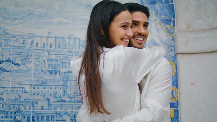 Smiling sweethearts embracing at tile wall place close up. Two enamoured lovers feeling happy enjoying romantic date. Cheerful latina woman hugging boyfriend looking distance. Loving people bonding Royalty-Free Stock Footage #1101761239