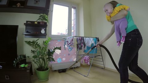 woman with baby on her hands cleaning floor with vacuum cleaner. Wide angle shot. 4K UHD.