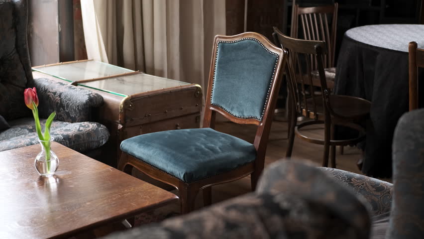 old retro vintage wooden armchair with blue upholstery stands in front of table with flower in old interior. concept of new flower and old furniture, comparison of eras and ages. Royalty-Free Stock Footage #1101775419