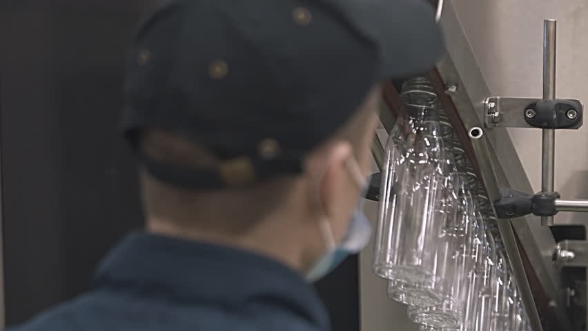 Factory worker inserting the empty plastic bottles into the machine. Factory worker attaches multiple bottles on the manufacturing equipment. Factory worker placing bottles on the production line.