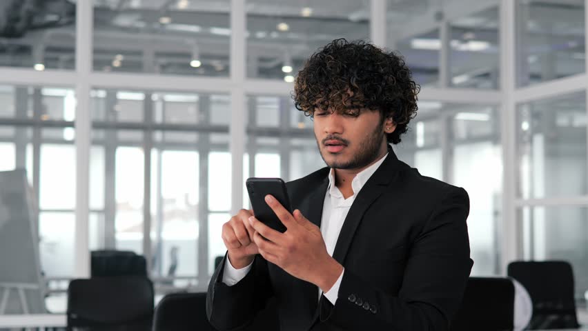 Latino man reading very bad news on mobile phone in an office. Businessman shocked, disappointed, possibly due to a contract breach and financial loss. Emotional impact of negative events in business. Royalty-Free Stock Footage #1101781945
