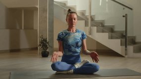 A young woman in a blue sports uniform finishes her meditation and rolls up her yoga mat. A video in which a woman finishes her morning yoga workout and leaves to get ready for work.