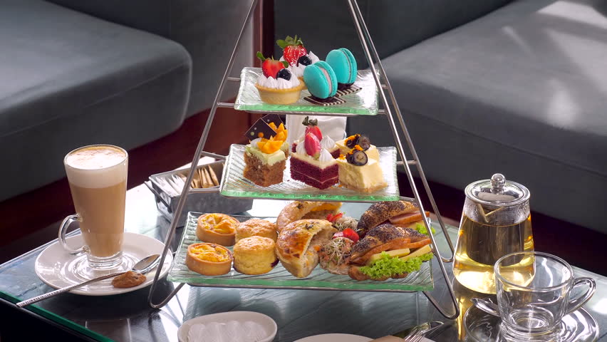 Elegant afternoon tea setup, complete with tiered trays of fresh sandwiches, pies, berry cakes and miniature fruit tarts with tea and coffee set. Delicious sweet food.