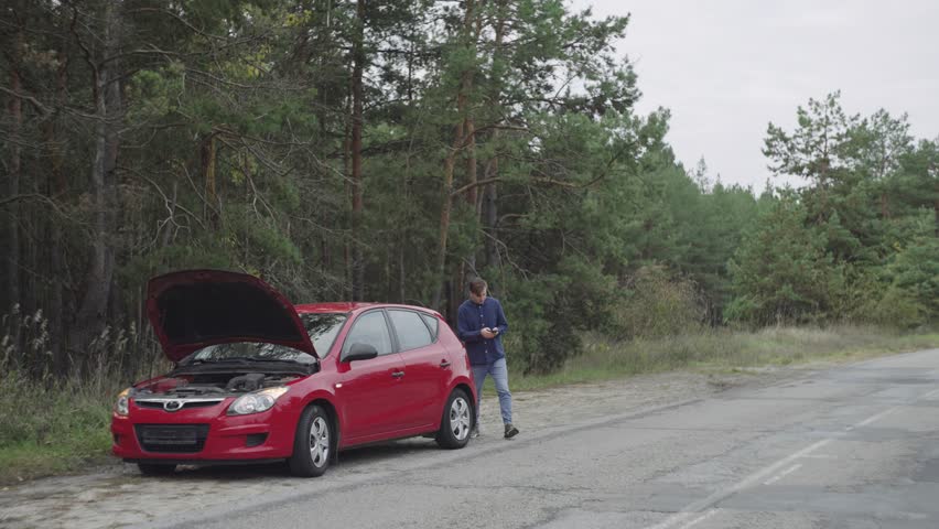 A man calls for help on the phone, the car breaks down, malfunction. A guy talks on the phone about a broken car. Road adventure, need technical support. High quality 4k footage Royalty-Free Stock Footage #1101785469