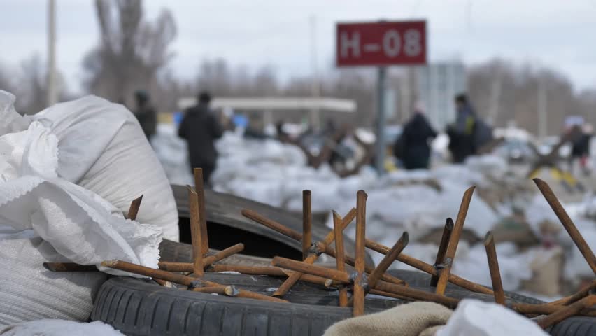 A close plan of home -made metal spikes lying on a barrekad, consisting of bags of sand and old car tires. Behind a blurry view of the block post. Russian-Ukrainian war.