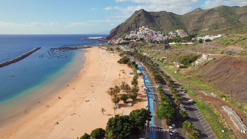 Aerial view of the Las Teresitas beach and San Andres resort town in Tenerife, Canary Islands, Spain. Yellow sand beach, palm trees and coastal road. Drone backward dolly shot Royalty-Free Stock Footage #1101785911