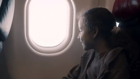 A charming girl is sitting at the window of the plane, the child looks out the window of the airplane during the flight. A teenage girl is flying in an airplane and is sitting by the window. 4K - Powered by Shutterstock - Get 15% off with code: PIKWIZARD15