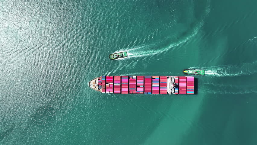 Aerial top view of  Cargo Container Ship with Tug boat carrying container and running very fast for export cargo from container yard port to custom ,Contrail line in the ocean