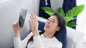 Happy young asian woman relaxing at home. Female smile lying on sofa and holding mobile smartphone. Girl using video call to friend
