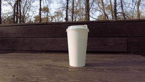 white paper cup with coffee on a wooden bench at sunset