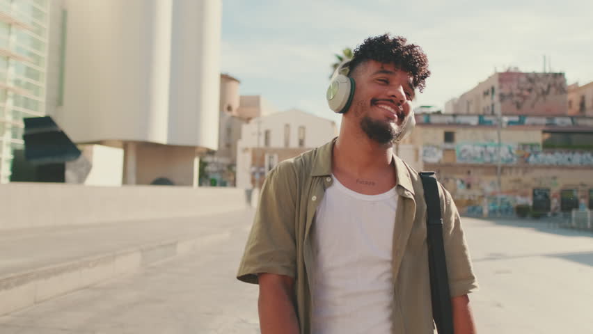 Young man with beard in an olive-colored shirt listens to music on headphones, dances