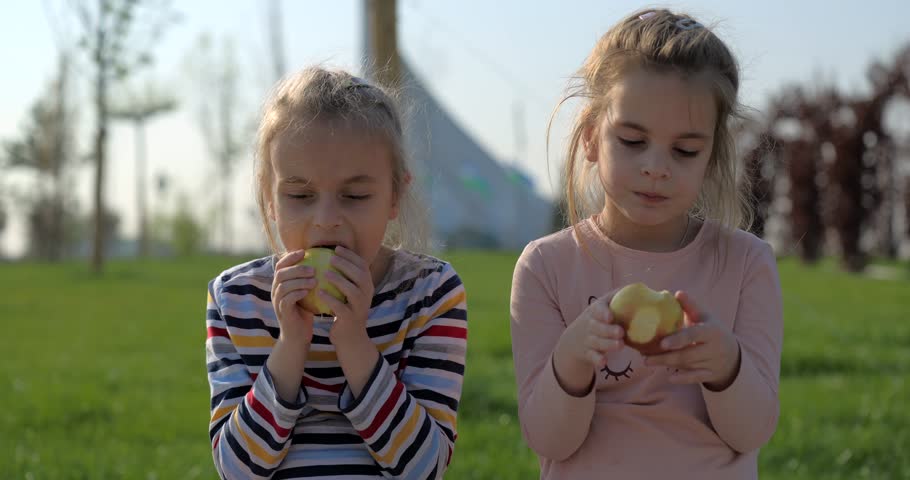 Two cute girls eating apples outdoor