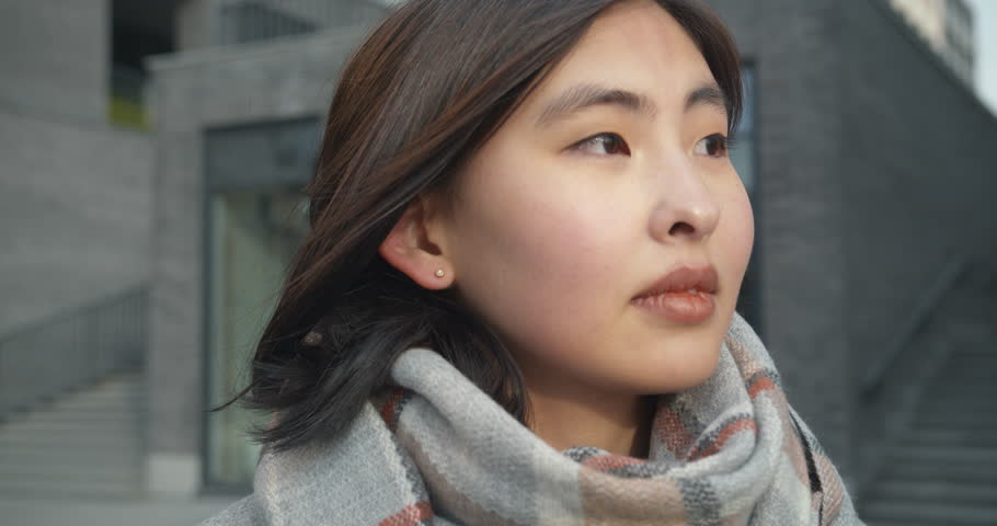 Close-up of woman face. Portrait of a beautiful young Asian woman standing against the background of a plain gray business center in a coat. Fashion, beauty. Portraits.