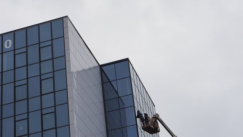 Working on a hydraulic lift repairing a glass wall of a building