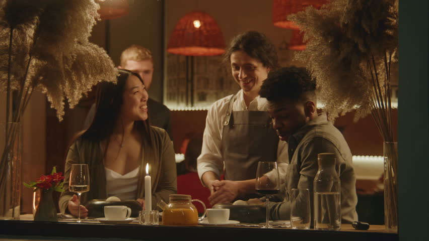 African american man and asian woman sit in modern gastro cafe together. The chef serves delicious dishes in flambe style. Happy multi ethnic couple on a date in restaurant. Concept of public eating. Royalty-Free Stock Footage #1101812667