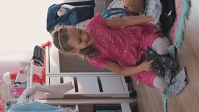 Vertical video. Happy little girl having fun by making a mess in her room, throwing her clothes up in the air, slow motion