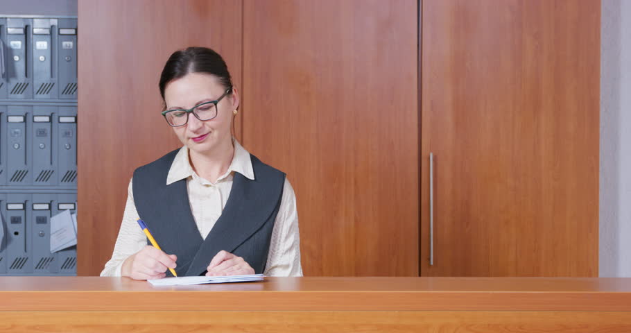 Behind reception desk, an administrator in formal clothes and glasses welcomes dog with money. Guest check-in at dog-friendly hotel reception desk. The client brought money to bank for safekeeping Royalty-Free Stock Footage #1101830513