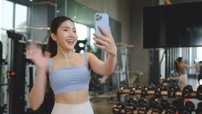 Young asian athletic woman with perfect body wearing sportswear making video call with smart phone to friends or family to show her achievements and results while workout in gym, healthy lifestyle