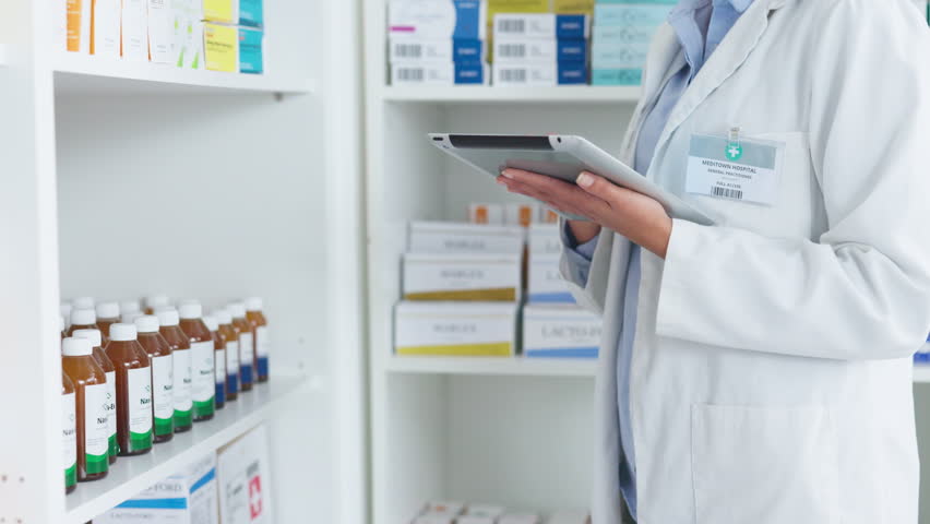 Pharmacist using digital tablet while checking prescription medication at a pharmacy. Medical professional, chemist or pharmaceutical worker doing inventory of medicine stock at a healthcare clinic