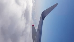 Flying above the clouds - view of passenger jet aircraft wing and winglet against clear blue sky. Vertical video clip with copy space.
