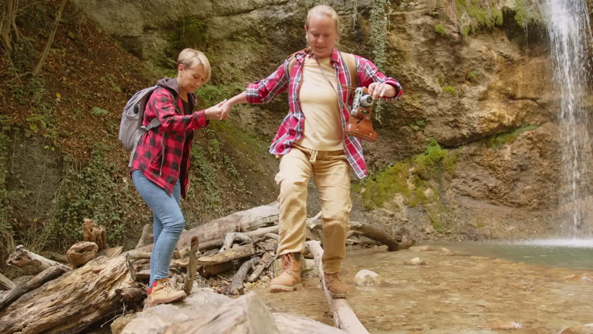 Traveler women friends adventure wild highlands walking on stones of mountain stream near waterfall. | Shutterstock HD Video #1101842259