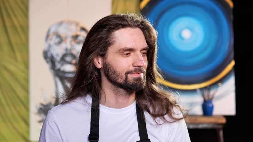 Handsome artist exuding creative spirit of an artist at work. His long, flowing hair adds to his artistic vibe, while his white t-shirt keeps the focus on his art. Man having charming healthy smile.