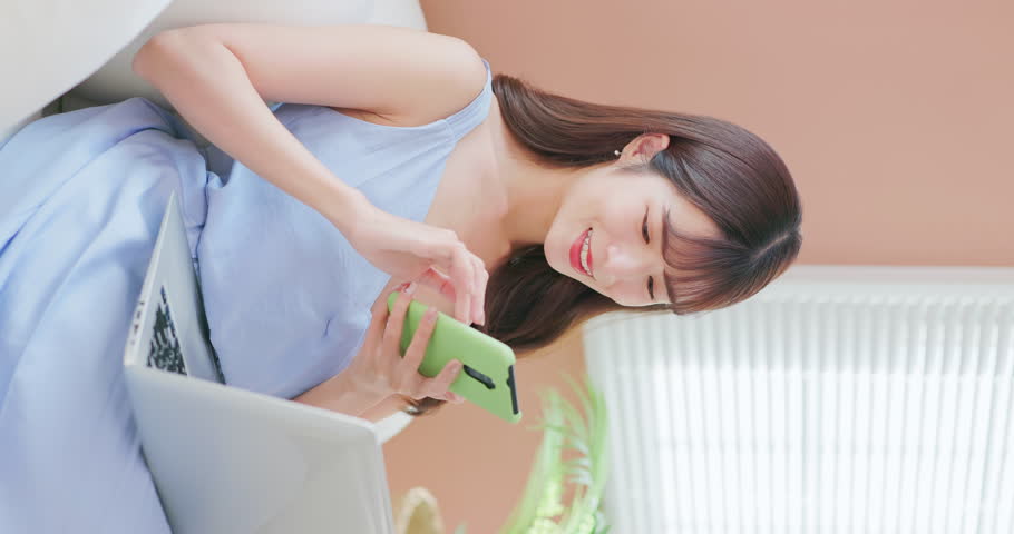 vertical asian girl using her phone and notebook easily sitting on a comfortable sofa