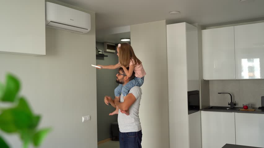 Father kept on shoulders little daughter and turn on air conditioner using remote control. Happy family adjust comfortable temperature of cooler system Royalty-Free Stock Footage #1101846073